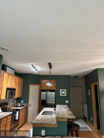 2460 119th Ct NE Unit D, Blaine, MN 55449 - kitchen featuring stainless steel appliances, a textured ceiling, light wood-type flooring, a kitchen island with sink, and brown cabinets