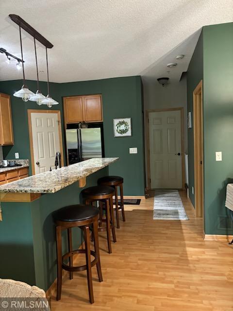 2460 119th Ct NE Unit D, Blaine, MN 55449 - kitchen featuring stainless steel fridge with ice dispenser, light wood-type flooring, a breakfast bar area, brown cabinetry, and a center island with sink