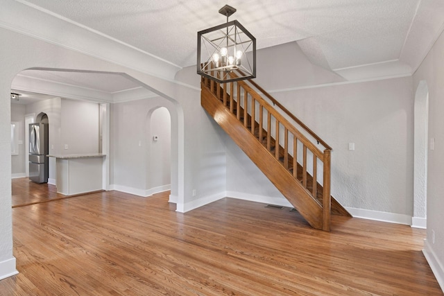 3305 Huntington Ave, Saint Louis Park, MN 55416 - unfurnished living room featuring arched walkways, a chandelier, wood finished floors, stairway, and a textured ceiling