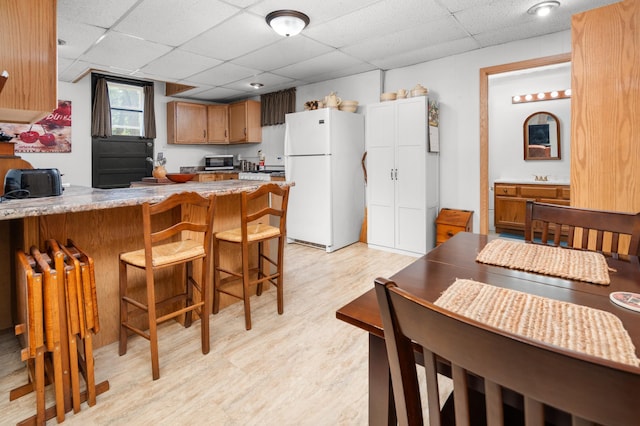 1708 Woodland Rd, Saint Cloud, MN 56304 - kitchen featuring freestanding refrigerator, a peninsula, a drop ceiling, light wood finished floors, and a breakfast bar
