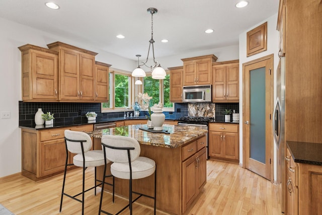 3027 135th Ave NE, Ham Lake, MN 55304 - kitchen featuring appliances with stainless steel finishes, a kitchen island, light wood-style floors, brown cabinetry, and a breakfast bar