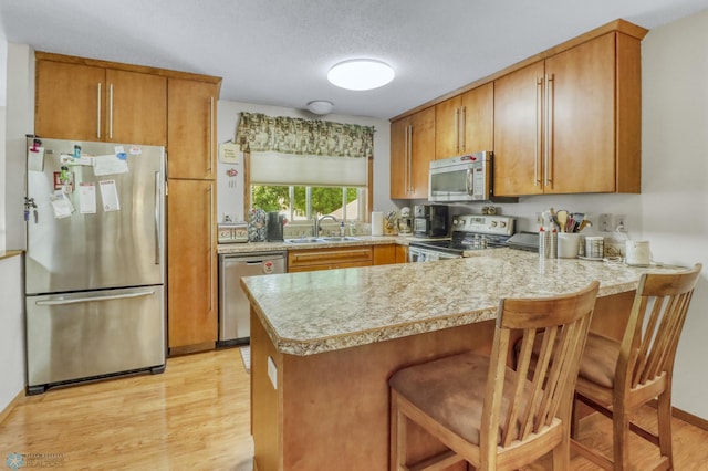 2744 32nd St S, Moorhead, MN 56560 - kitchen featuring stainless steel appliances, a peninsula, brown cabinetry, light wood-type flooring, and a textured ceiling