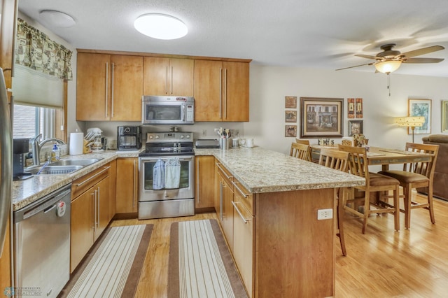 2744 32nd St S, Moorhead, MN 56560 - kitchen featuring appliances with stainless steel finishes, a peninsula, light wood-type flooring, and brown cabinets
