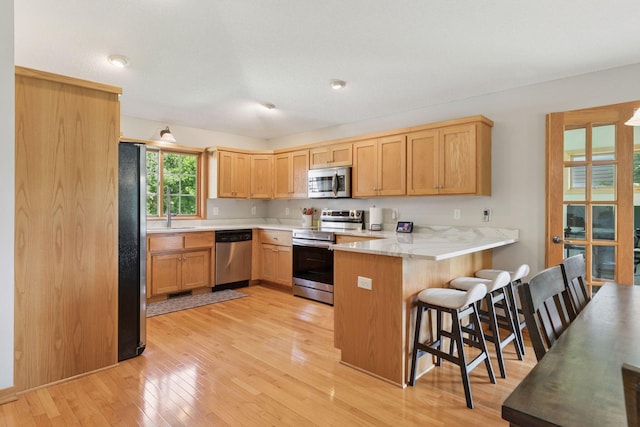 15450 Goodview Ave N, Hugo, MN 55038 - kitchen with stainless steel appliances, a peninsula, light wood-style flooring, light countertops, and a kitchen bar
