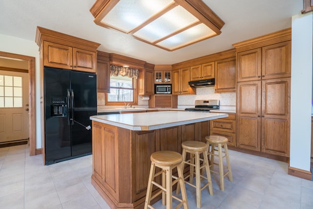 1757 325th Ave, West Sweden Twp, WI 54837 - kitchen featuring stainless steel appliances, brown cabinetry, under cabinet range hood, a center island, and light countertops