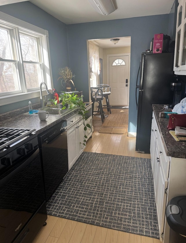 338 Jefferson St, Saint Croix Falls, WI 54024 - kitchen with stove, black dishwasher, light wood finished floors, white cabinets, and glass insert cabinets