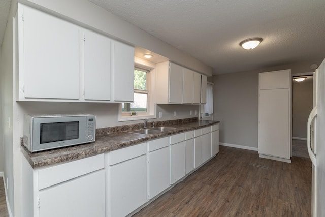 269 Chestnut St, Ellsworth, WI 54011 - kitchen with white microwave, dark wood finished floors, a textured ceiling, white cabinets, and dark countertops