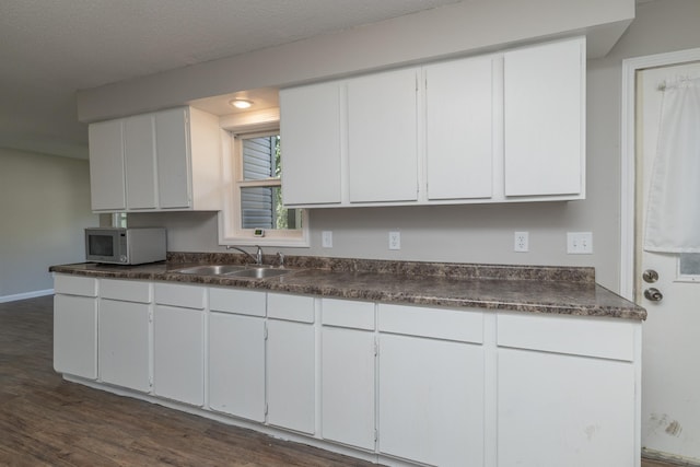269 Chestnut St, Ellsworth, WI 54011 - kitchen with white microwave, dark countertops, dark wood-style floors, and white cabinets