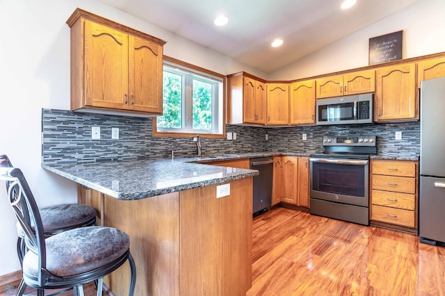 152 17th Ave W, West Fargo, ND 58078 - kitchen with stainless steel appliances, a peninsula, vaulted ceiling, dark stone countertops, and a breakfast bar
