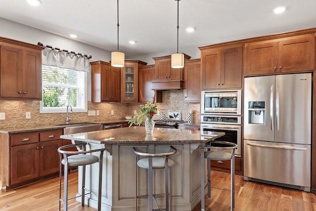 9871 7th St N, Lake Elmo, MN 55042 - kitchen featuring stainless steel appliances, brown cabinetry, a kitchen bar, light wood-type flooring, and recessed lighting