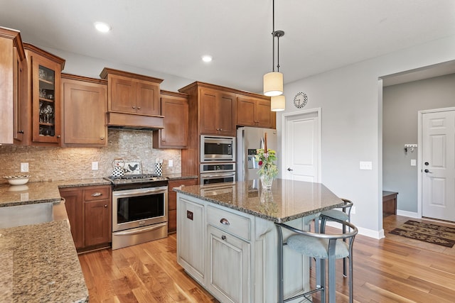9871 7th St N, Lake Elmo, MN 55042 - kitchen with stainless steel appliances, a kitchen breakfast bar, under cabinet range hood, brown cabinetry, and recessed lighting