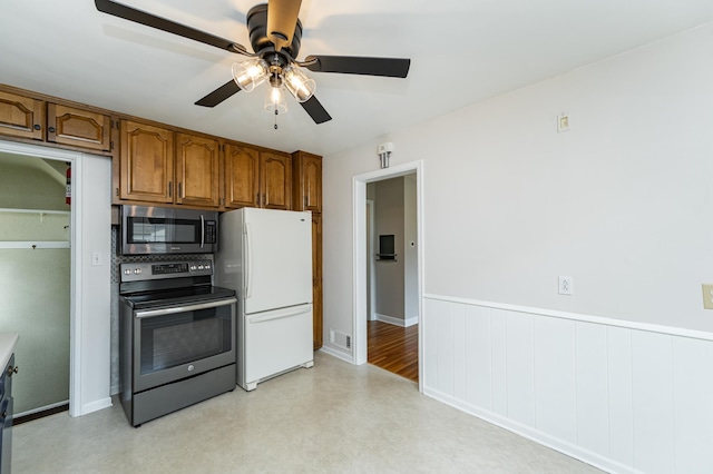 1007 12th Ave NE, Rochester, MN 55906 - kitchen featuring appliances with stainless steel finishes, brown cabinetry, ceiling fan, a wainscoted wall, and light flooring