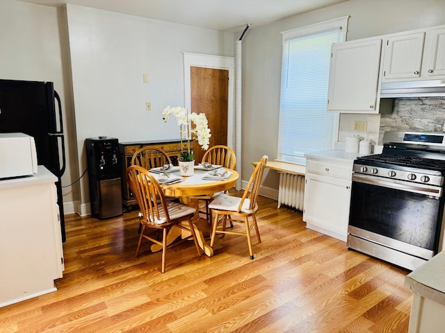 371 Sherburne Ave, Saint Paul, MN 55103 - kitchen with stainless steel gas range, radiator heating unit, light countertops, white cabinetry, and under cabinet range hood