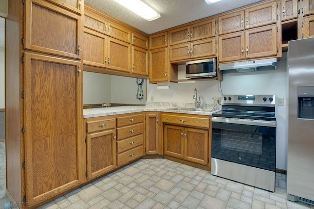 604 2nd Ave S, Kindred, ND 58052 - kitchen with stainless steel appliances, brown cabinets, brick patterned floors, and under cabinet range hood
