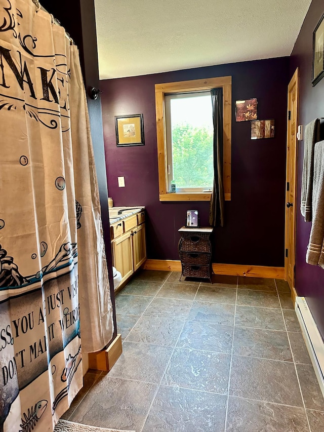 316 2nd St NE, Menahga, MN 56464 - full bath with baseboard heating, vanity, stone tile flooring, and a textured ceiling