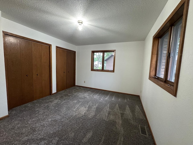 605 Arbor Ct, Marshall, MN 56258 - unfurnished bedroom featuring two closets, dark carpet, and a textured ceiling