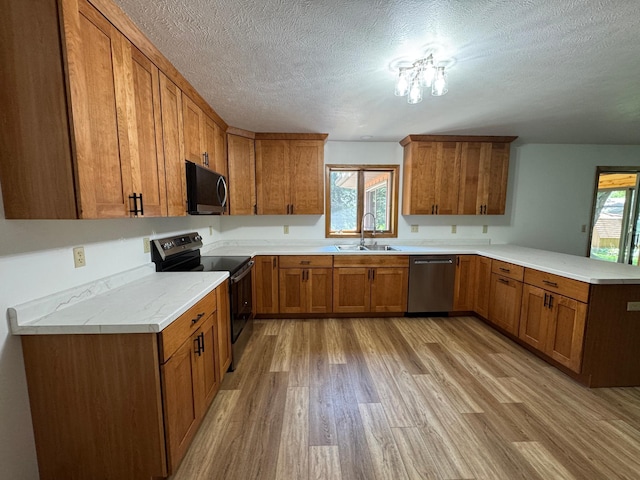 605 Arbor Ct, Marshall, MN 56258 - kitchen with stainless steel appliances, a peninsula, brown cabinetry, light wood finished floors, and a textured ceiling