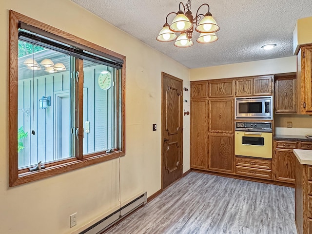 607 1st St, Marshall, MN 56258 - kitchen featuring white oven, stainless steel microwave, light wood-style floors, a chandelier, and brown cabinets