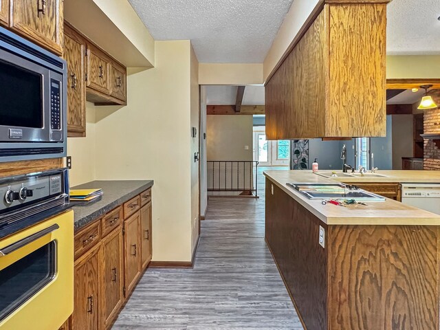 607 1st St, Marshall, MN 56258 - kitchen with stainless steel appliances, wood finished floors, a textured ceiling, brown cabinets, and a peninsula