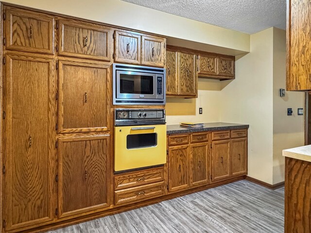 607 1st St, Marshall, MN 56258 - kitchen with oven, stainless steel microwave, light wood-style flooring, a textured ceiling, and brown cabinetry