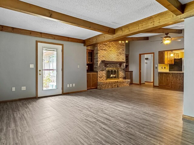 607 1st St, Marshall, MN 56258 - unfurnished living room featuring wood finished floors, ceiling fan, a textured ceiling, a fireplace, and beam ceiling