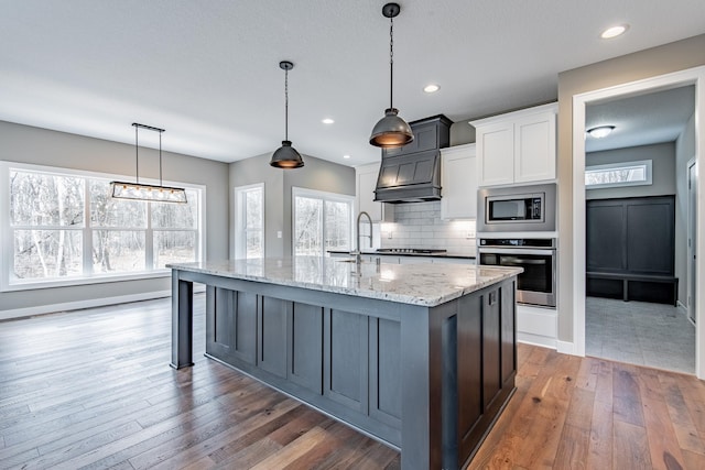 51440 Long Point Pl, Shamrock Twp, MN 55760 - kitchen featuring appliances with stainless steel finishes, light stone counters, hardwood / wood-style flooring, a kitchen island with sink, and tasteful backsplash