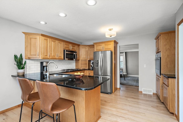 1890 Sheridan Ave, Saint Paul, MN 55116 - kitchen featuring stainless steel appliances, a peninsula, decorative backsplash, a kitchen breakfast bar, and light wood-type flooring