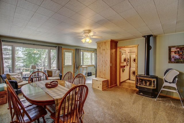 37566 Tulaby Lake Dr, Waubun, MN 56589 - carpeted dining room with stacked washer / dryer, a wood stove, wood walls, and a ceiling fan