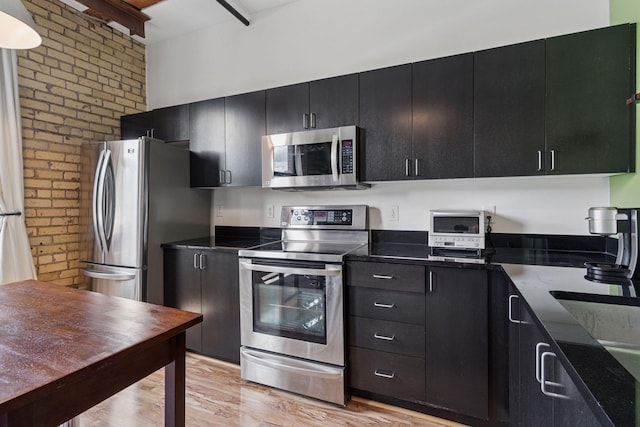 406 Wacouta St Unit 611, Saint Paul, MN 55101 - kitchen with appliances with stainless steel finishes, brick wall, dark cabinetry, light wood-style floors, and dark stone counters
