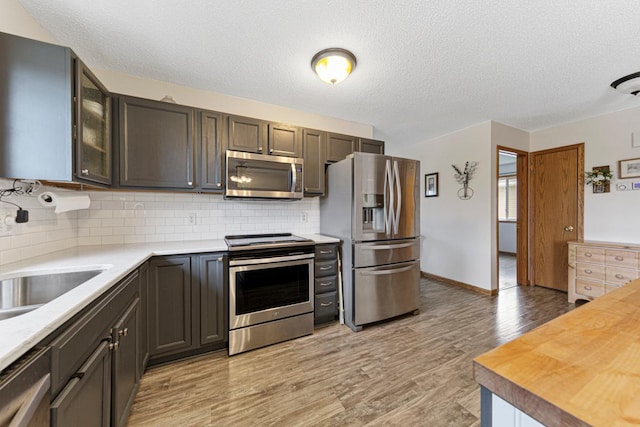 2115 Turpin St, Saint Peter, MN 56082 - kitchen featuring appliances with stainless steel finishes, backsplash, light wood-style flooring, glass insert cabinets, and a textured ceiling