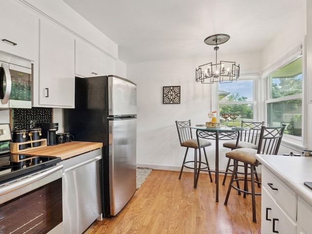 910 62nd St, Minneapolis, MN 55419 - kitchen with appliances with stainless steel finishes, a chandelier, light wood-style floors, white cabinetry, and pendant lighting