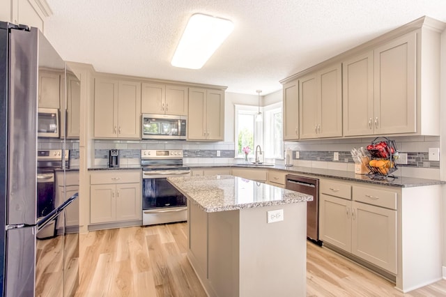 141 145th Ln NE, Ham Lake, MN 55304 - kitchen featuring appliances with stainless steel finishes, light wood finished floors, backsplash, light stone countertops, and a kitchen island