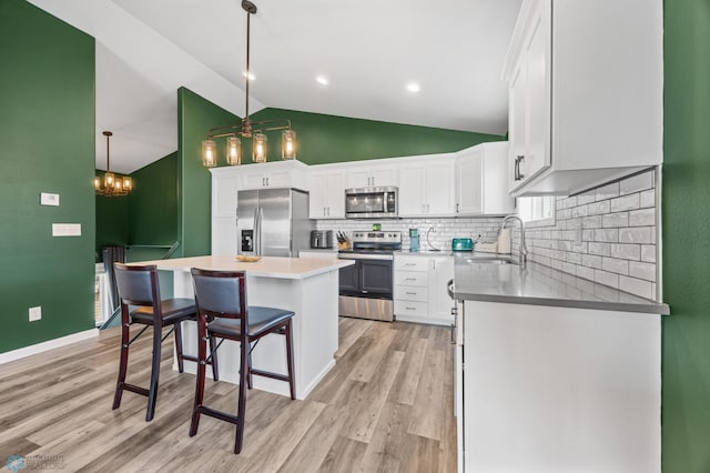 1009 Highland Ln W, West Fargo, ND 58078 - kitchen featuring appliances with stainless steel finishes, vaulted ceiling, white cabinets, tasteful backsplash, and light wood-style flooring