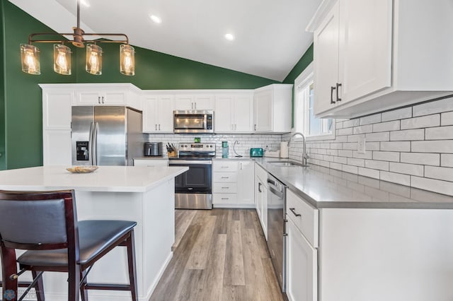 1009 Highland Ln W, West Fargo, ND 58078 - kitchen featuring appliances with stainless steel finishes, white cabinetry, vaulted ceiling, light wood-type flooring, and a kitchen bar