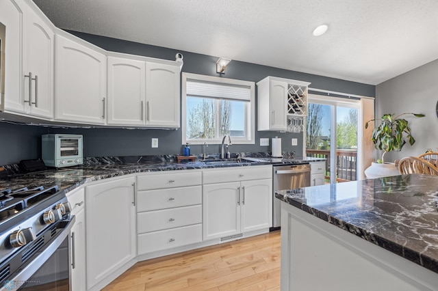 1623 10th St W, West Fargo, ND 58078 - kitchen featuring appliances with stainless steel finishes, light wood-style flooring, dark stone counters, white cabinetry, and plenty of natural light