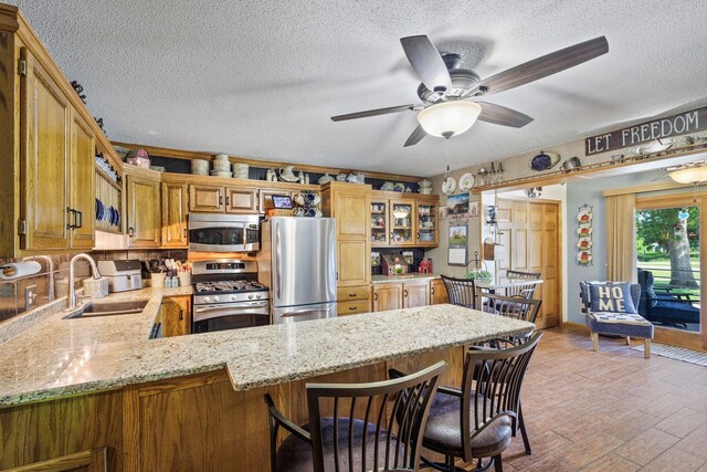 28040 Csah 25, Swede Grove Twp, MN 56243 - kitchen with appliances with stainless steel finishes, a peninsula, a textured ceiling, a ceiling fan, and light stone counters