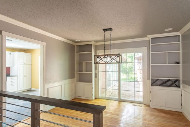 2321 17th Ave S, Fargo, ND 58103 - unfurnished dining area featuring light wood-style floors, a textured ceiling, crown molding, wainscoting, and a decorative wall