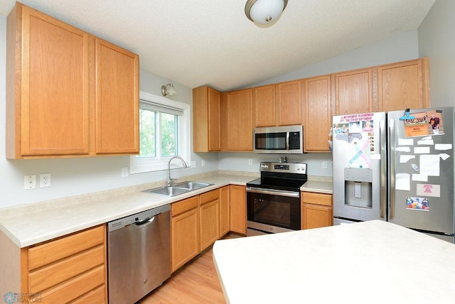 2441 60th Ave S, Fargo, ND 58104 - kitchen with stainless steel appliances, vaulted ceiling, light wood finished floors, light countertops, and light brown cabinetry