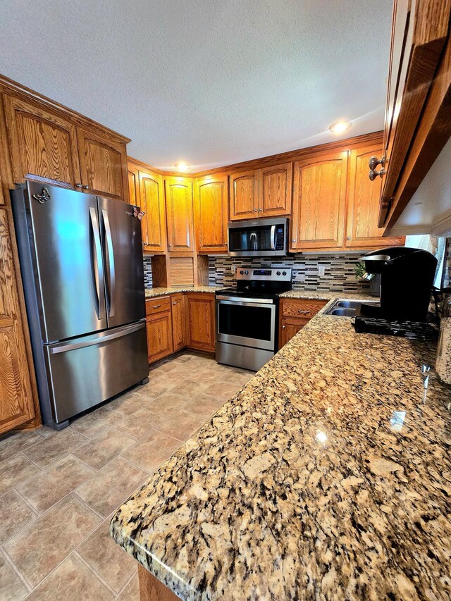 8047 Ingleside Ave S, Cottage Grove, MN 55016 - kitchen with appliances with stainless steel finishes, brown cabinetry, backsplash, light stone counters, and a textured ceiling