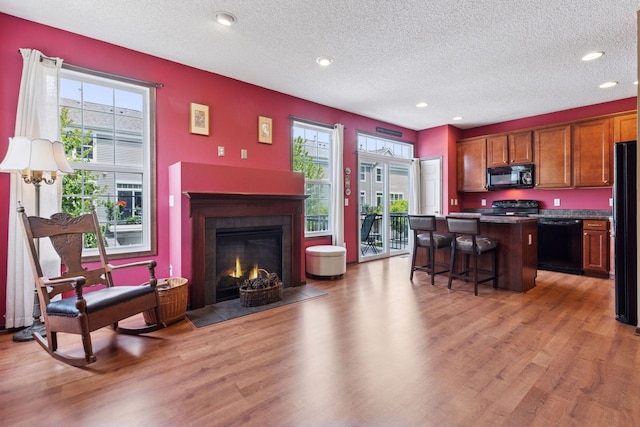 5214 Scott Ct, Robbinsdale, MN 55422 - kitchen with black appliances, a breakfast bar area, a kitchen island, light wood-style flooring, and a textured ceiling