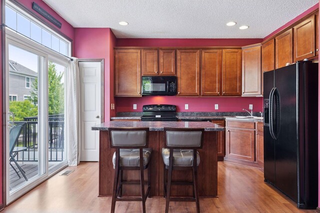 5214 Scott Ct, Robbinsdale, MN 55422 - kitchen with black appliances, light wood finished floors, a textured ceiling, a kitchen island, and a kitchen bar