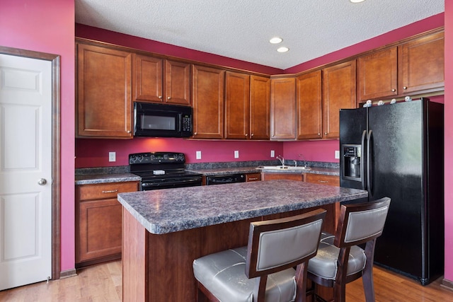 5214 Scott Ct, Robbinsdale, MN 55422 - kitchen with black appliances, a kitchen bar, light wood-style flooring, dark countertops, and a textured ceiling