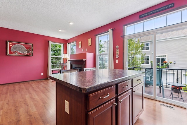 5214 Scott Ct, Robbinsdale, MN 55422 - kitchen with light wood-style flooring, dark countertops, a fireplace, a textured ceiling, and a center island