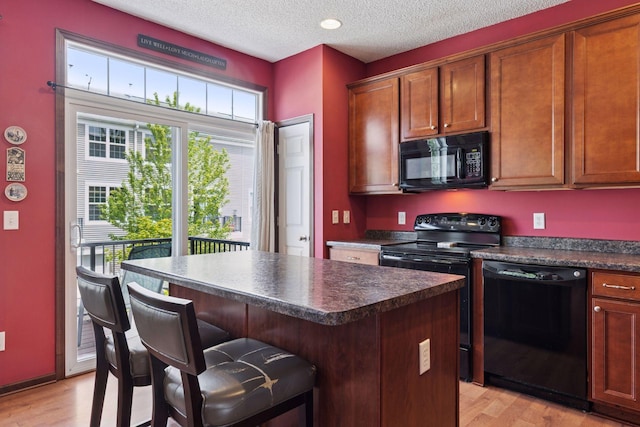 5214 Scott Ct, Robbinsdale, MN 55422 - kitchen featuring black appliances, dark countertops, light wood-type flooring, a kitchen breakfast bar, and a textured ceiling