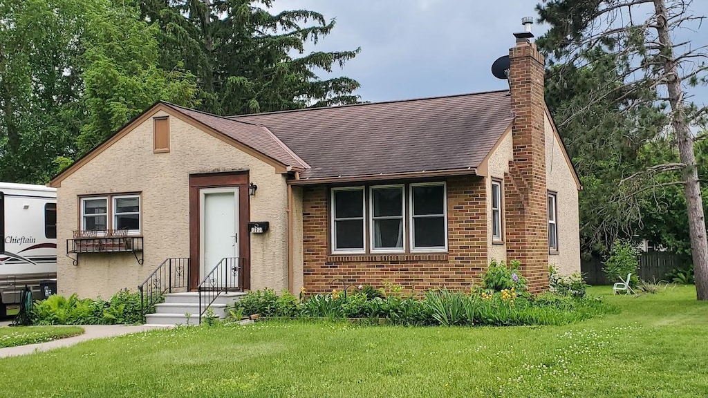 2122 Lacrosse Ave, Saint Paul, MN 55119 - view of front of house with a chimney, a front yard, roof with shingles, brick siding, and stucco siding