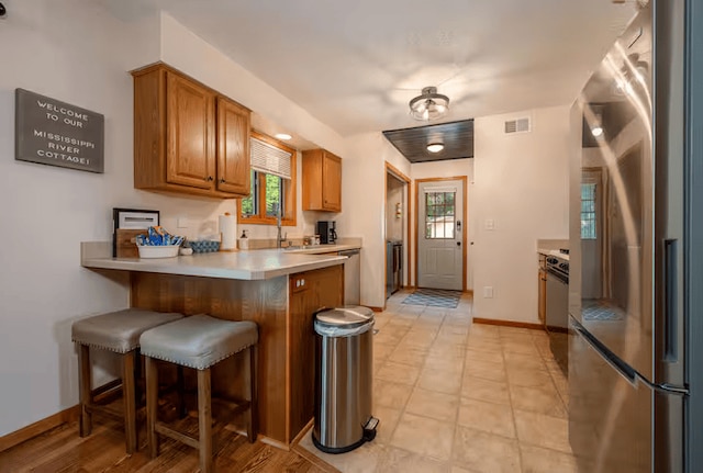 25463 County Road 267, Cohasset, MN 55721 - kitchen with a peninsula, a kitchen breakfast bar, brown cabinets, stainless steel refrigerator, and light countertops