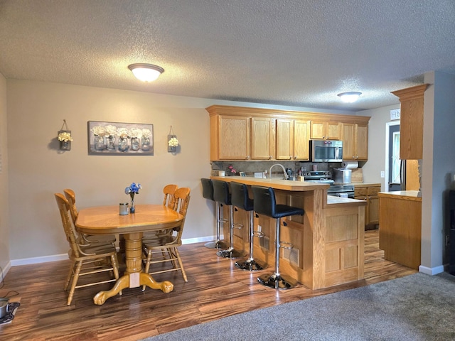 11348 Ibis St NW, Coon Rapids, MN 55433 - kitchen featuring appliances with stainless steel finishes, a peninsula, light countertops, a kitchen bar, and a textured ceiling