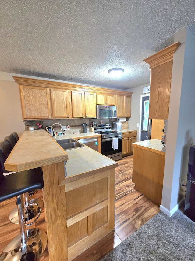 11348 Ibis St NW, Coon Rapids, MN 55433 - kitchen with stainless steel appliances, a peninsula, a breakfast bar area, tasteful backsplash, and tile countertops