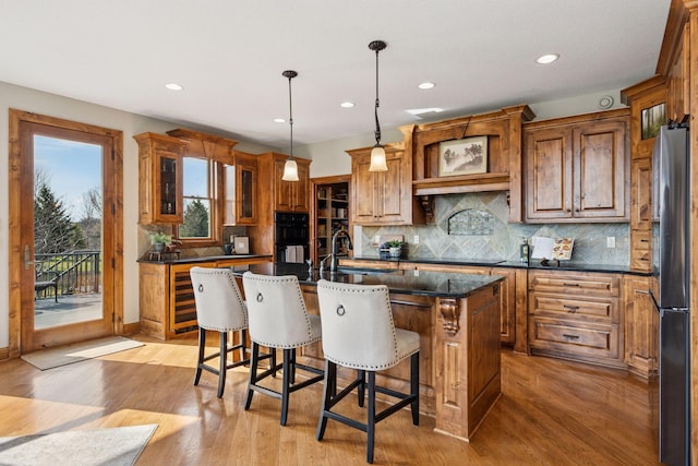 7530 Quail Ridge Trl, Greenfield, MN 55373 - kitchen featuring freestanding refrigerator, brown cabinetry, recessed lighting, a kitchen island with sink, and light wood-type flooring
