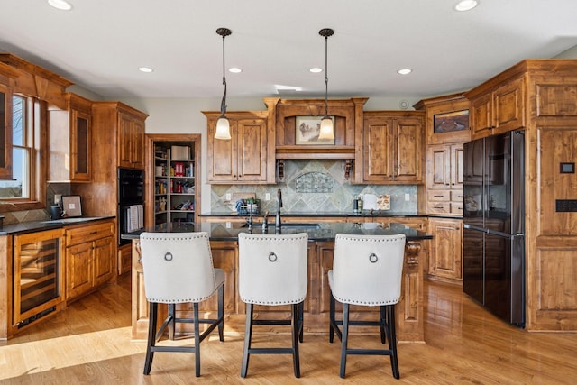 7530 Quail Ridge Trl, Greenfield, MN 55373 - kitchen with black appliances, beverage cooler, brown cabinets, a kitchen island with sink, and glass insert cabinets